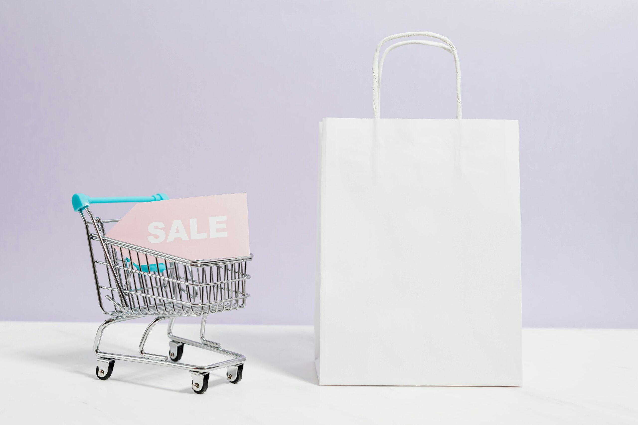 A miniature shopping cart with a sale sign beside a paper bag, perfect for online shopping themes.