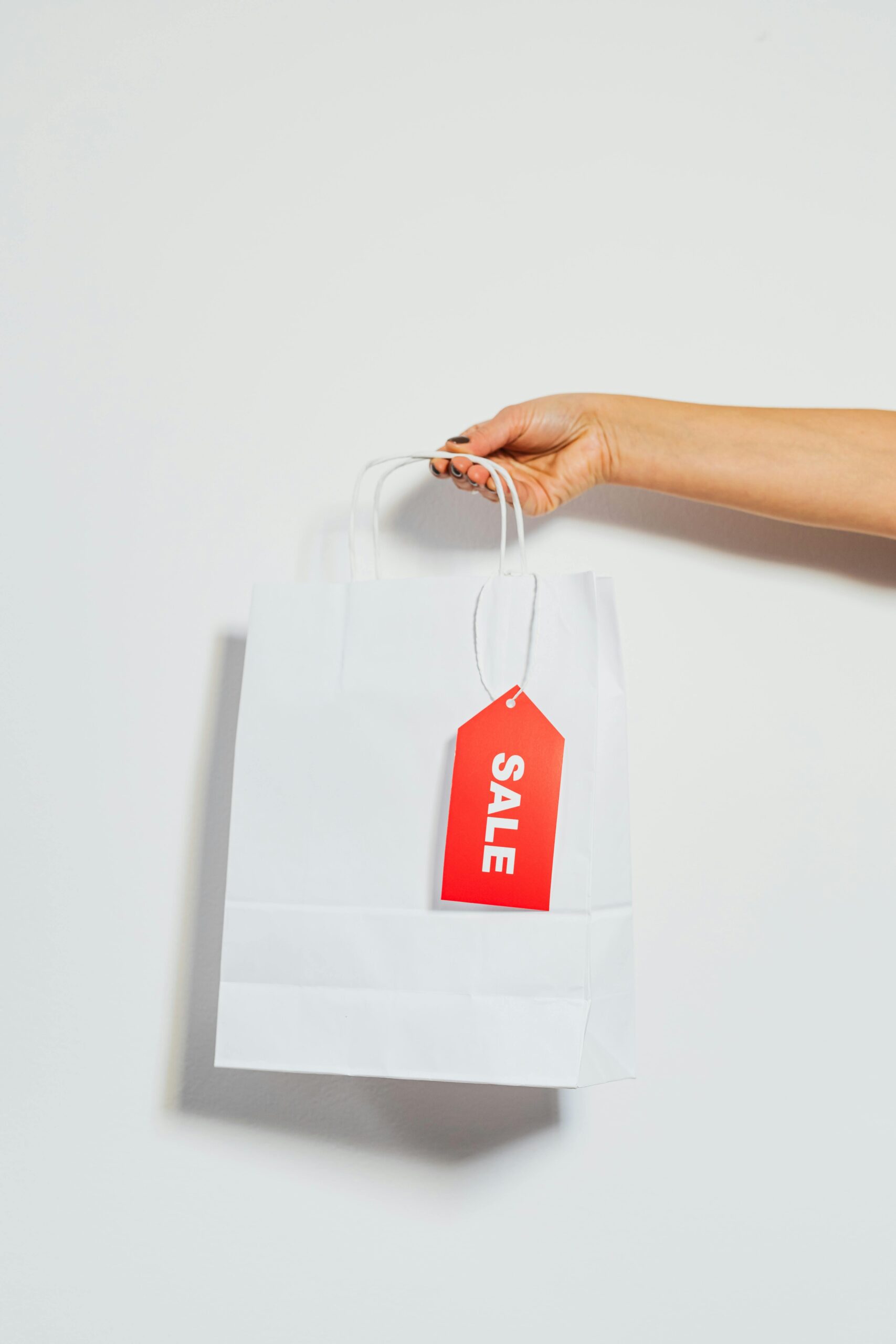 A person's hand holding a white shopping bag with a red sale tag on a white background.